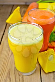 Two tall glasses of pumpkin and carrot juice, chopped vegetables on a wooden boards background