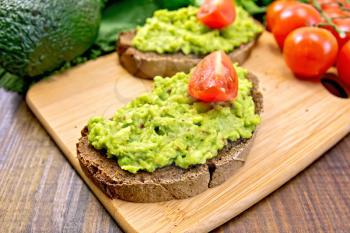 Two slices of rye bread with guakomole and tomato, avocado on the background dark wooden boards