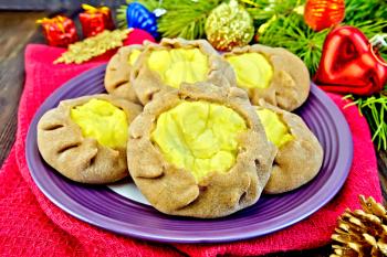 Carols with potato stuffed with rye flour in a plate on a red napkin, Christmas decorations, fir branches against a background of dark wooden board