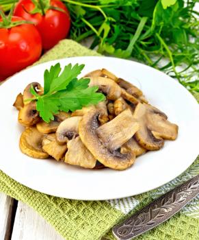 Champignons fried in a plate with parsley leaf, fork, tomatoes on a green napkin on the background light wooden boards