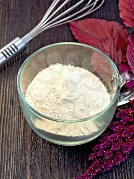 Amaranth flour in a glass cup with mixer, purple amaranth flower on the background of wooden boards