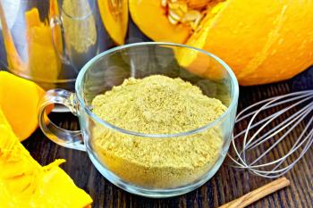 Flour pumpkin in a glass cup, sieve, mixer and cinnamon, fresh yellow pumpkin on a wooden boards background