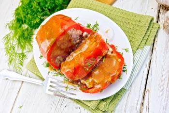 Sweet pepper stuffed with meat and rice with tomato sauce in the plate on a green napkin, fork, dill, parsley on the background light wooden boards