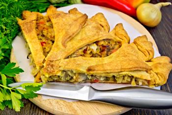 Pie with cabbage, sorrel and sweet pepper, knife, onion, parsley on a wooden boards background