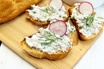 Bread with pate of cottage cheese, dill and radish on a wooden board, a napkin on the background light wooden table