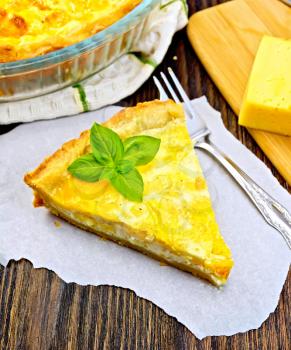 Tart with cheese, leek and sour cream and egg cream on paper, fork, cheese on a dark wooden board