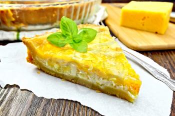 Tart with cheese, leek and sour cream and egg cream on paper, fork, cheese on a wooden boards background