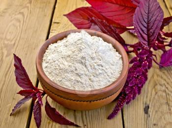 Amaranth flour in a clay bowl, purple amaranth flower on the background of a wooden table
