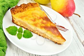 One slice of pear cake with cream sauce in white plate, fork, pear and mint, napkin on the background light wooden boards