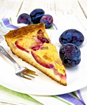Pie with plums and sour cream, fork on the plate on a kitchen towel on the background of wooden boards