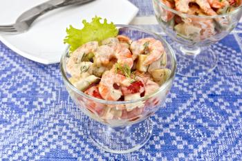 Salad with shrimp, avocado, tomatoes, green lettuce in a glass goblet, a plate against the background of a blue tablecloth