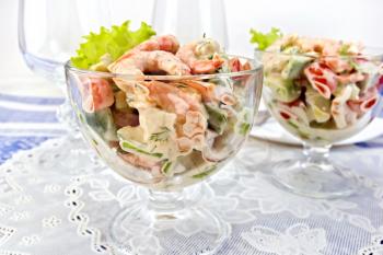 Salad with shrimp, avocado, tomato and mayonnaise, green lettuce in a glass goblet on a napkin, a plate against the background of blue linen tablecloth