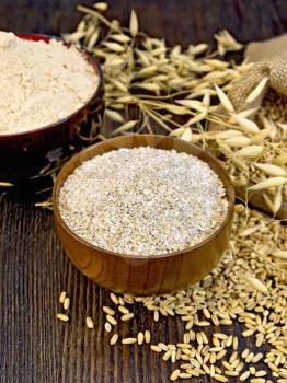 Bran flakes oat and oat flour in two wooden bowl, a bag of grain oats, oat ears on the background of wooden boards