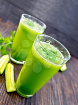 Cucumber juice in two tall glasses, cucumber and parsley on a dark wooden board
