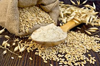Flour oat in a wooden spoon, a bag of oat, stalks of oats on the background of wooden boards