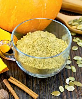 Flour pumpkin in a glass cup, rolling pin, spoon, nutmeg and cinnamon, fresh pumpkin, pumpkin seeds on the background of wooden boards