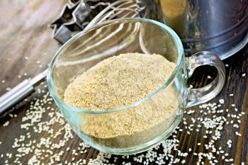 Sesame flour in a glass cup with sieve, mixer and molds for cookies, sesame seeds on a wooden boards background