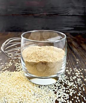 Sesame flour in a glass and mixer on the background of wooden boards
