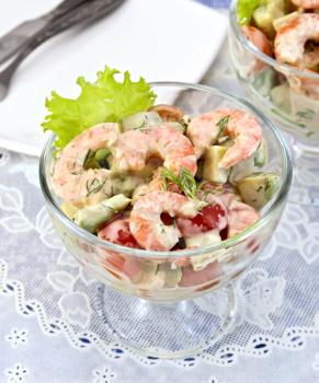 Salad with shrimp, avocado, tomato and mayonnaise, green lettuce in a glass goblet on a white napkin, a plate against the background of blue linen tablecloth