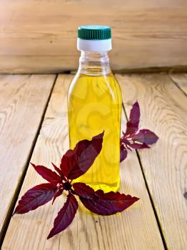 One plastic bottle of oil with a branch burgundy amaranth on background light wooden boards