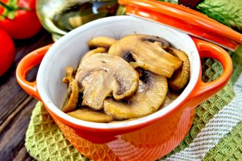 Champignons fried in a red ceramic pot on a napkin, garlic, dill and pomidoryna background wooden plank