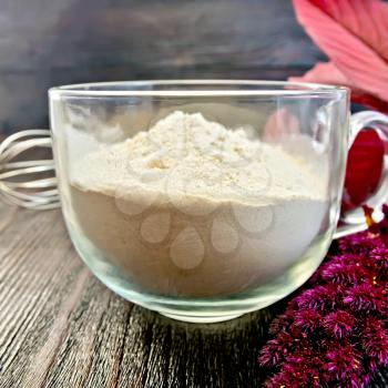 Amaranth flour in a glass cup with a mixer, purple amaranth flower on a background of wooden boards