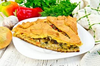 Pie with cabbage, sorrel and sweet peppers in a white plate, napkin, parsley on the background light wooden boards