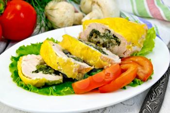 Roll of chicken breast with spinach, mushrooms and cheese on green salad in a white plate with slices of tomato, a napkin on a wooden boards background