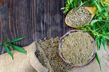 Flour in a clay bowl and hemp seeds in a spoon, green twigs of cannabis on sackcloth background on wooden board