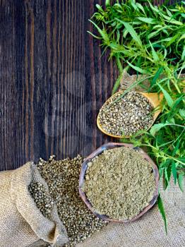 Flour in a bowl and hemp seeds in a spoon, green twigs of cannabis on sackcloth background on dark wooden board