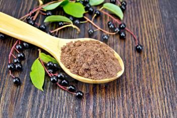 Flour of bird-cherry in a spoon with black berries and green leaves on a background of wooden boards