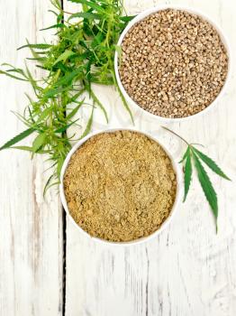 Flour and hemp seed in white bowls, cannabis leaves on the background of the wooden planks on top