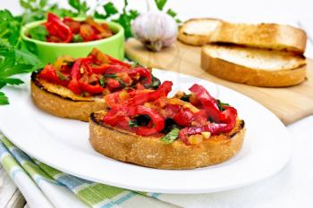 Bruschetta with roasted tomatoes, peppers, garlic, onions and parsley in a plate on a napkin against the background of wooden boards
