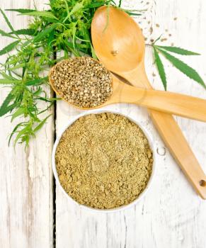 Hemp flour in bowl, grain in spoon, cannabis leaves on the background of the wooden boards top