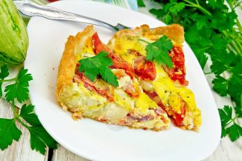 Two pieces pie of zucchini with tomatoes and eggs in a plate on a napkin, parsley on the background light wooden boards