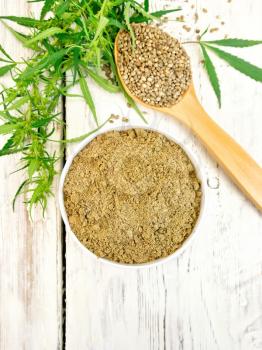 Hemp flour in white bowl, grain in spoon, cannabis leaves on the background of the wooden planks on top