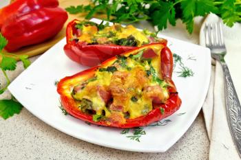 Sweet pepper stuffed with sausage, egg and cheese with dill in white plate, napkin, fork and parsley on a background of a granite table