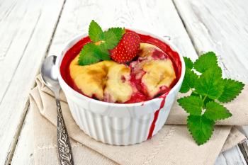 Strawberry pudding in a bowl with berries and mint on a napkin against the background of the wooden planks