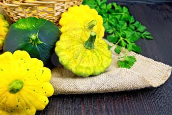 Yellow and green squash on sackcloth and wicker basket, a bunch of parsley on a wooden boards background