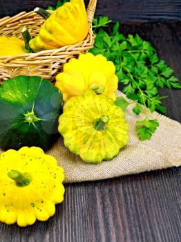 Yellow and green squash on sackcloth and wicker basket, a bunch of parsley on a dark wooden board