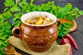 Roast with chicken, potatoes, squash, and sweet peppers in a portion clay pot on a napkin of burlap, spoon, parsley on a wooden table background