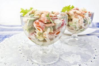 Salad with shrimp, avocado, tomato and mayonnaise, green salad in a glass goblet on a white napkin against a background of blue linen tablecloth