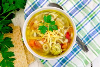 Minestrone soup with meat, celery, tomatoes, zucchini and cabbage, green peas, carrots and pasta, sprinkled grated cheese in a bowl on a towel on the background of wooden board top