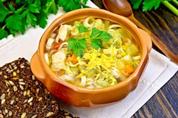 Minestrone soup with meat, celery, tomatoes, zucchini and cabbage, green peas, carrots and pasta in an earthenware bowl, cheese, bread on a dark wooden board