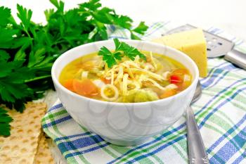 Minestrone soup with meat, celery, tomatoes, zucchini and cabbage, green peas, carrots and pasta, sprinkled grated cheese in a bowl on a towel on the background of a wooden board