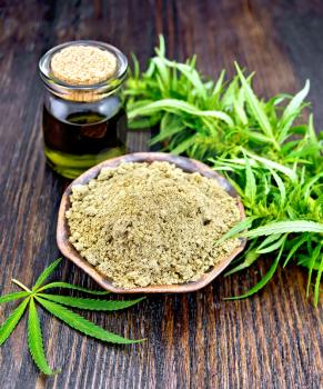 Hemp flour in a clay bowl in a glass jar oil, cannabis leaf on a background of wooden boards