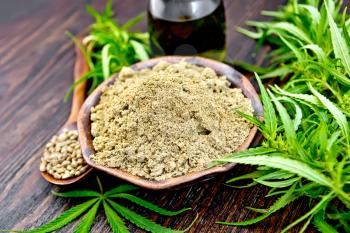 Hemp flour in a clay bowl, grain in a spoon in a glass jar oil, cannabis leaves on the background of wooden boards