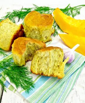 Pumpkin Scones with garlic and dill on a towel, yellow pumpkin slices on the background light wooden boards