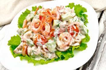 Salad with shrimp, avocado, tomatoes and mayonnaise on the green lettuce in the plate, napkin, fork on the background light wooden table