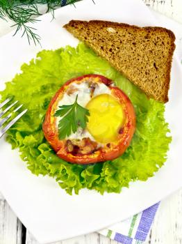 Scrambled eggs with ham and mushrooms in a tomato on a green lettuce in the plate, bread, fork and a napkin on the background light wooden boards on top